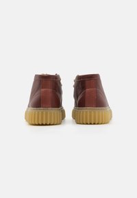 Brown leather ankle boots with a textured finish, featuring a rear elastic panel and a rubber sole with vertical grooves.