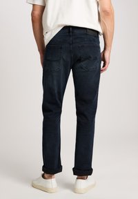 Donkerblauwe denim jeans met een slim fit, voorzien van twee achterzakken en opgerolde boorden. Draagt met witte schoenen.