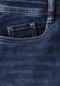 Mörkblå denimjeans med kontrasterande beige sömmar. Funktioner inkluderar en framficka och en mjuk textur.