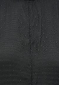 Black textured fabric featuring a honeycomb pattern with small raised dots, designed for stretch and breathability. Smooth neckline.