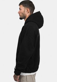 Sort hættetrøje lavet af blødt stof, med en rummelig hætte, ribbede manchetter og en afslappet pasform. Minimalistisk design uden synlige logoer.