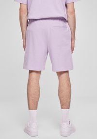 Lilla bomullsblandede shorts med elastisk midje, sidelommer og en enkelt baklomme; brukt med hvite joggesko og sokker.