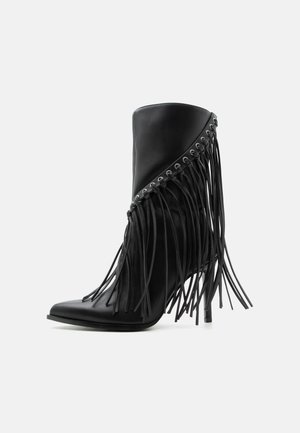 Sort ankelstøvle med høje hæle, skrå frynser og metaløjer langs den øverste kant, spids tå og stiletthæl.