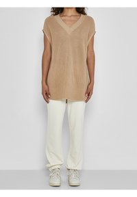 Beige pletený oversized top s V-výstřihem a krátkými rukávy, spárovaný s krémovými tepláky a světlými teniskami. Jednoduchý, strukturovaný design.