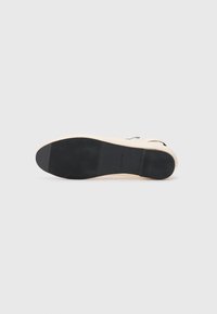 Sandale plate beige avec semelle en caoutchouc noir présentant une texture antidérapante et un petit talon, exposée sur fond blanc.