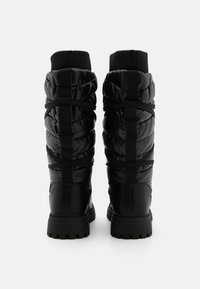 Black padded ankle boots with a sleek finish, elastic straps, and textured knit cuffs, featuring a rugged rubber outsole for traction.