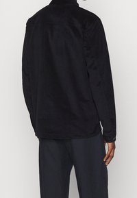 Camicia in corduroy nera con colletto, maniche lunghe e polsini con bottoni; presenta una vestibilità rilassata e una texture sottile. Vista posteriore mostrata.