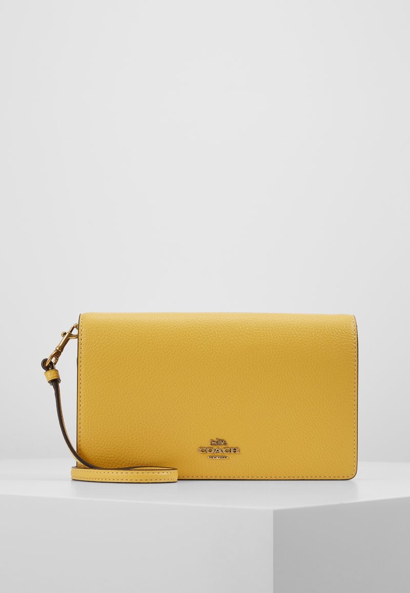 Sac bandoulière en cuir jaune à texture granuleuse, avec une quincaillerie dorée, un design aplati et une bandoulière amovible ornée d'un accent logo.