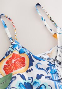 Robe à bretelles fines à motifs floraux et fruités avec des détails bleus et orange, gros plan sur l'encolure et l'étiquette de la marque "NEXT".