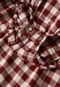 Tela de cuadros rojos y blancos con un patrón de espiga, con un escote fruncido y botones metálicos. Material de algodón texturizado.