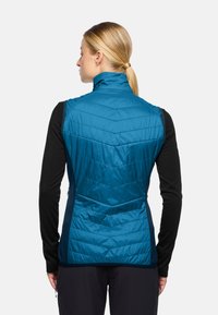 Ärmelleste blaue isolierte Weste mit hohem Kragen, ausgestattet mit Zickzack-Steppung und seitlichen Einsätzen in einer kontrastierenden dunkleren Farbe.