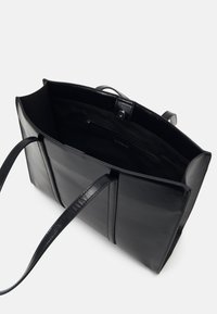 Sort læder tote taske med et rummeligt interiør, der har en lynlåslomme og solide, flade håndtag. Glat tekstur og enkelt design.