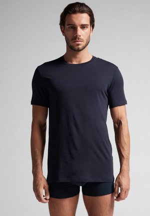 Camiseta de manga corta azul marino, con un diseño ajustado, fabricada en un tejido suave y con cuello redondo. Combinada con pantalones cortos negros ajustados.