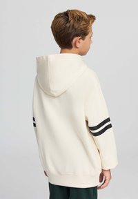 Felpa leggera crema con un motivo a doppia striscia nera sulle maniche. Presenta una tasca a marsupio e un cappuccio regolabile con coulisse.