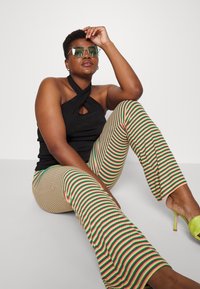 Top preto de halter com detalhe em forma de chave, calças largas às riscas multicolores e óculos de sol verdes. Alças finas e tecido texturizado.
