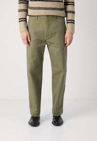 Olive green cotton trousers with a relaxed fit, featuring a button closure and subtle side pockets, paired with a striped sweater.