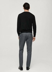Maglione nero, pantaloni grigi su misura, design minimale, texture liscia, luce sottile nel tessuto. Scarpe nere completano l'outfit.