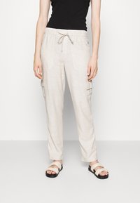 Lichtbeige cargobroek met een trekkoord in de taille, twee zijzakken en een relaxte pasvorm, gecombineerd met beige sandaaltjes met bandjes.