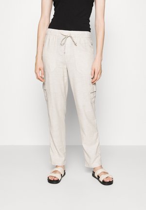 Pantalons cargo beige clair avec une taille à cordon, deux poches latérales et une coupe décontractée, associés à des sandales à lanières beiges.