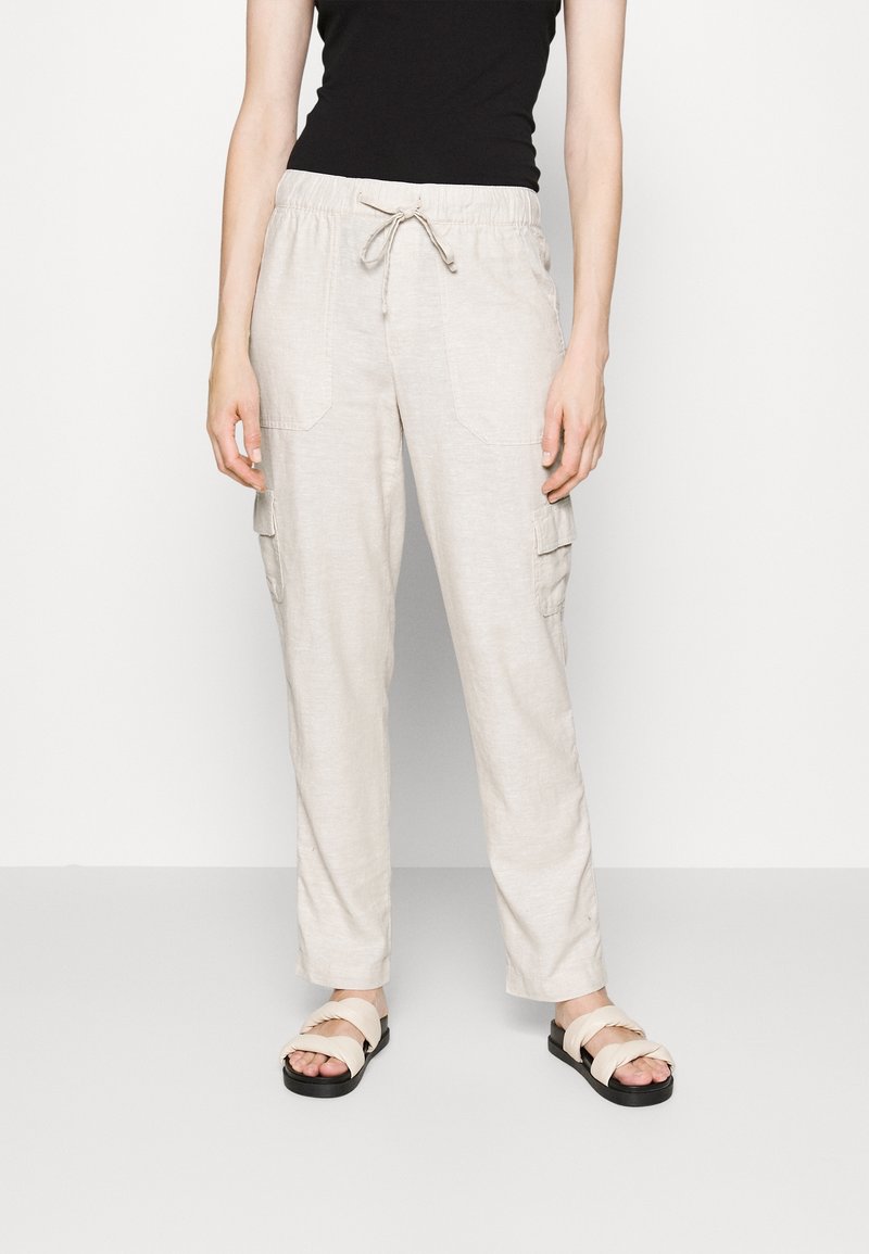 Lichtbeige cargobroek met een trekkoord in de taille, twee zijzakken en een relaxte pasvorm, gecombineerd met beige sandaaltjes met bandjes.