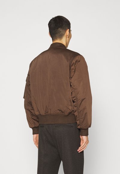 Jachetă bomber maro cu un design ușor căptușit, cu mansete și guler căptușit. Textură netedă, cu o croială lejeră și fără hardware vizibil.