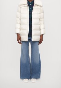 White puffer coat with a faux fur collar, featuring a zip front and side pockets, layered over a green plaid shirt and flared denim pants.