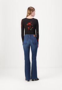 Bodysuit negro de manga larga con patrón floral en la parte delantera, combinado con unos vaqueros acampanados azules que tienen un parche de cuero marrón en la parte trasera de la cinturilla.