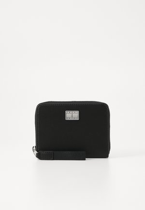 Monedero negro con forma rectangular, hecho de material suave, que cuenta con una placa de logo plateada y una correa desmontable para llevar.