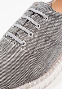 Botte en tissu rayé gris avec un bout rond, devant à lacets, œillets blancs et semelle texturée avec un détail de surpiqûre contrastante.