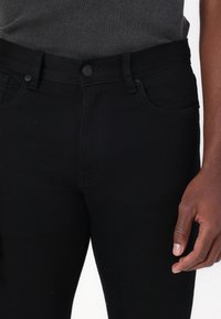 Black denim jeans with a slim fit, featuring front pockets, a button closure, and subtle stitching details. Smooth texture, mid-rise.