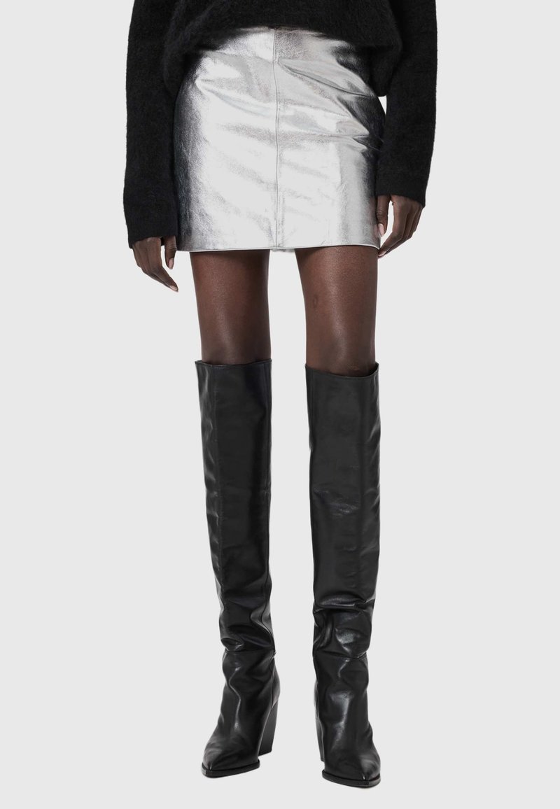 Sudraba metāliska mini svārki ar gludu faktūru, ar piegulošu siluetu. Kombinēti ar augstiem melniem ādas ceļgala zābakiem ar nelielu papēdi.