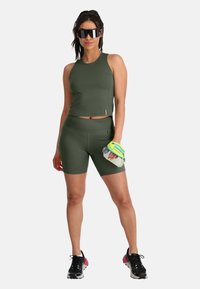 Donkergroen sporttanktop en shorts van rekbaar, vochtafvoerend materiaal; gecombineerd met zwarte sneakers en een waterfles.