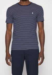 Námořnické a bíle pruhované tričko s kulatým výstřihem a krátkými rukávy. Obsahuje malé vyšívané logo na hrudi.