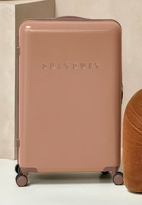 Rosa Hartschalenkoffer mit abgerundeten Ecken, geprägt mit dem "SUITSUIT"-Logo, vier drehbaren Rädern und einem strukturierten Griff oben.