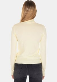 Maglione giallo chiaro aderente con maniche lunghe, polsini a costine e collo rotondo. Texture morbida, design minimalista, indossato con jeans scuri.