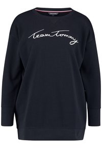 Černá mikina s širokým výstřihem a dlouhými rukávy. "Team Tommy" je vyšitý bílým kurzívním písmem v přední části. Měkká textura.