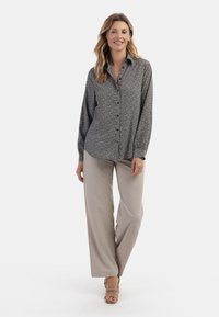 Camicia a maniche lunghe a righe bianche e nere, abbinata a pantaloni beige a gamba larga e sandali aperti. Tessuto dalla consistenza liscia.