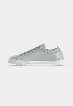 Baskets basses gris clair avec col élastique, œillets métalliques, semelle en caoutchouc blanche embossée, profil latéral sur fond uni.