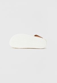 Sandalo marrone con tomaia testurizzata, dotato di chiusura con fibbia e suola bianca a onde. Il design è minimalista e flat.