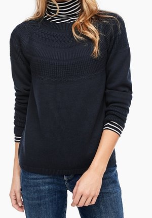 Pull en maille bleu marine avec des motifs texturés, dotés d'un col montant et de manches rayées. Associé à un jean bleu.