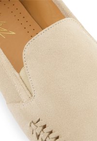Beige suède instappers met elastische zijkanten en stiksel op de neus, met een zachte bruine leren binnenzool met perforaties.