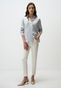 Hellbluse aus Satin mit Knopfverschluß, weiße Slim-Fit-Hose und beige Slingbacks. Glatte Textur und taillierte Passform.