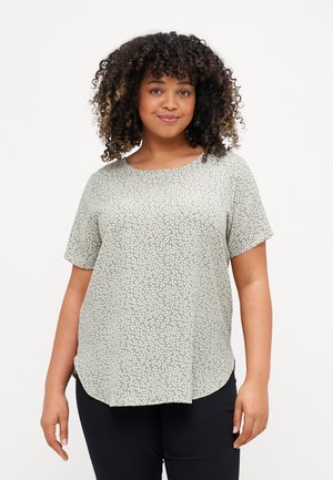 Top verde de manga corta con un patrón de piedras blancas, cuello redondo y dobladillo curvado. La tela parece suave y ligera.
