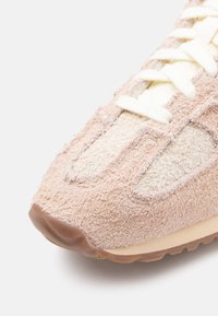 Light pink athletic shoe with textured fabric upper, cream accents, and a rubber sole. Laces are white, securing the shoe's fit.