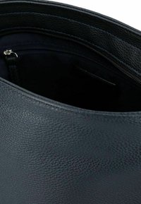 Bolso de mano de cuero negro con superficie texturizada, forma redondeada y cierre con cremallera. Vista interior que muestra un compartimento oscuro sin forro.