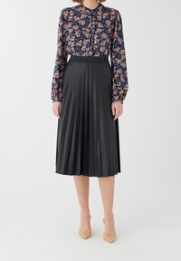 Gonna midi plissettata nera con una texture liscia, abbinata a una blusa floreale con tonalità di blu, rosa e verde su uno sfondo scuro.