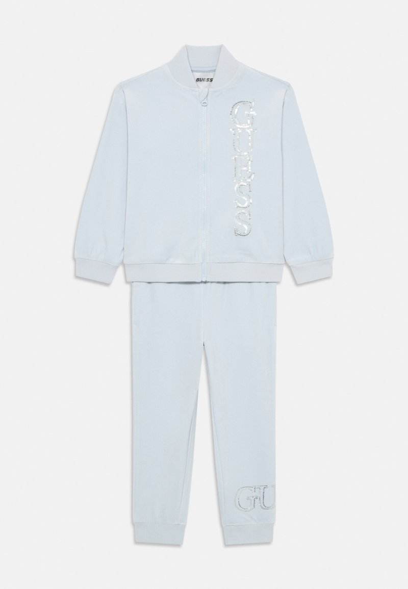 Jasnoniebieski zestaw dresowy składający się z kurtki na zamek z cekinowym logo „GUESS” oraz pasujących spodni z haftowanym detalem „G”. Miękka tkanina.