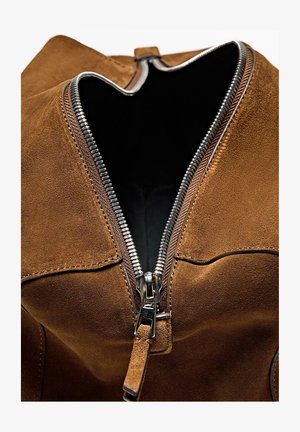 Sac en suede marron avec une fermeture éclair en métal argenté, présentant une large ouverture et une doublure intérieure lisse. Surface texturée et détail de fermeture éclair remarquable.