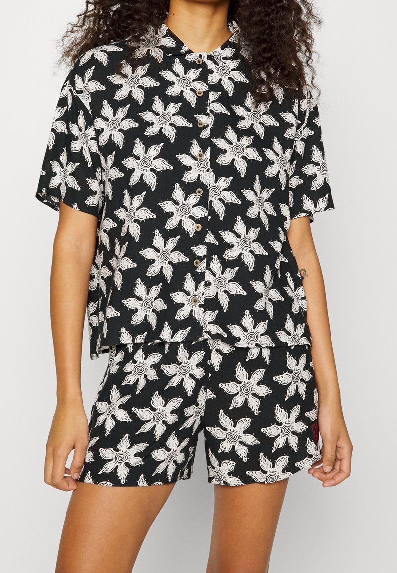 Ensemble en tissu noir avec motif floral blanc ; chemise à manches courtes à boutons et short assorti ; texture légère et respirante.