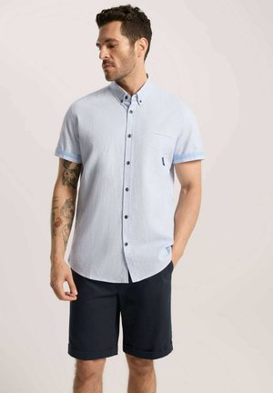 Jasnoniebieska, krótko rękawowa koszula zapinana na guziki z kieszonką, zestawiona z ciemnogranatowymi szortami. Posiada kontrastujące jasnoniebieskie mankiety i czarne guziki.